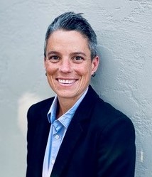 Photo of Suzy Requarth smiling, wearing a dark suit with a blue shirt.