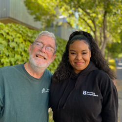 A man and a woman smile together outside on the sidewalk