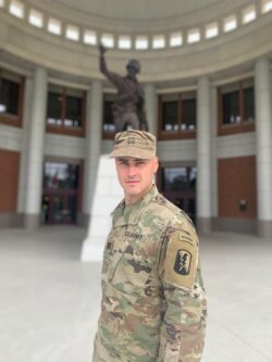 Steven Pavlov wearing a military uniform and smiling in front of a large military statue