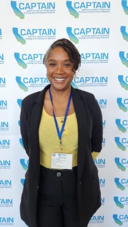 DDS employee stands in front of wall with blue words that say CAPTAIN