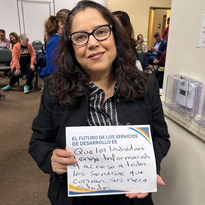 Josefina smiles at the camera while holding a sign that reads El Futuro de los Servicios de Desarollo es Que los individuos tengan información y acceso a todos los servicios que cubran sus necesidades