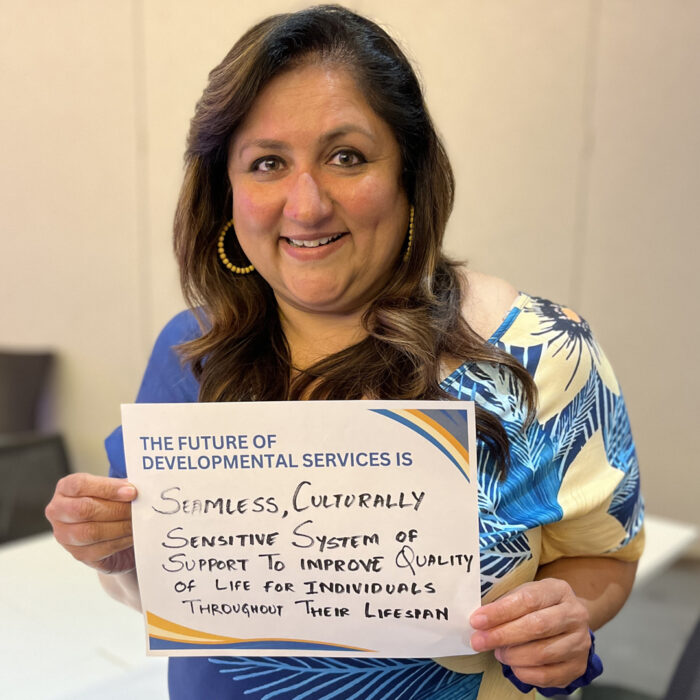Kavita Sreedhar smiles at the camera while holding a sign that reads The Future of Developmental Services is Seamless, Culturally Sensitive System of Support to Improve Quality of Life for Individuals throughout their Lifespan