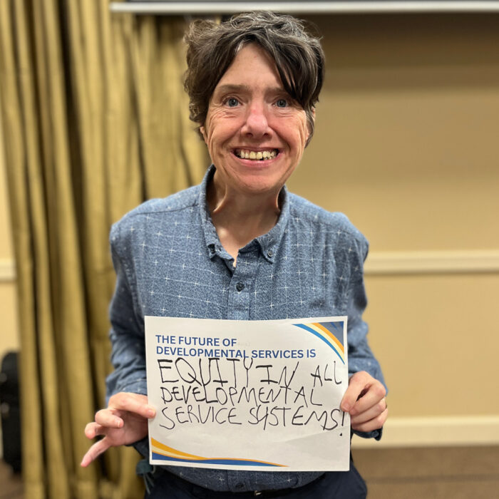 Kecia smiles at the camera while holding a sign that reads The Future of Developmental Services is equity in all developmental service systems