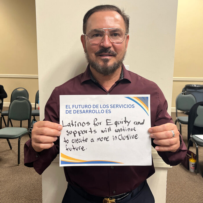 Joe Perales looks at the camera while holding a sign that reads: "El futuro de los servicios de desarrollo es: Latinos for equity and supports with continue to create a more inclusive future."