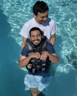 Man holds the back of a smiling man wearing a life vest in a pool