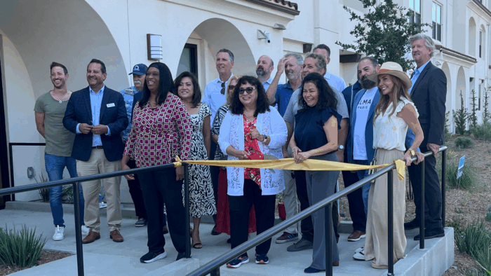 A group of people stand on a ramp leading on to a building and in front of a yellow ribbon