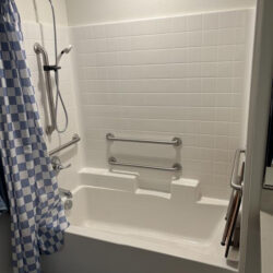 A bathtub with a checkered curtain and featuring safety bars
