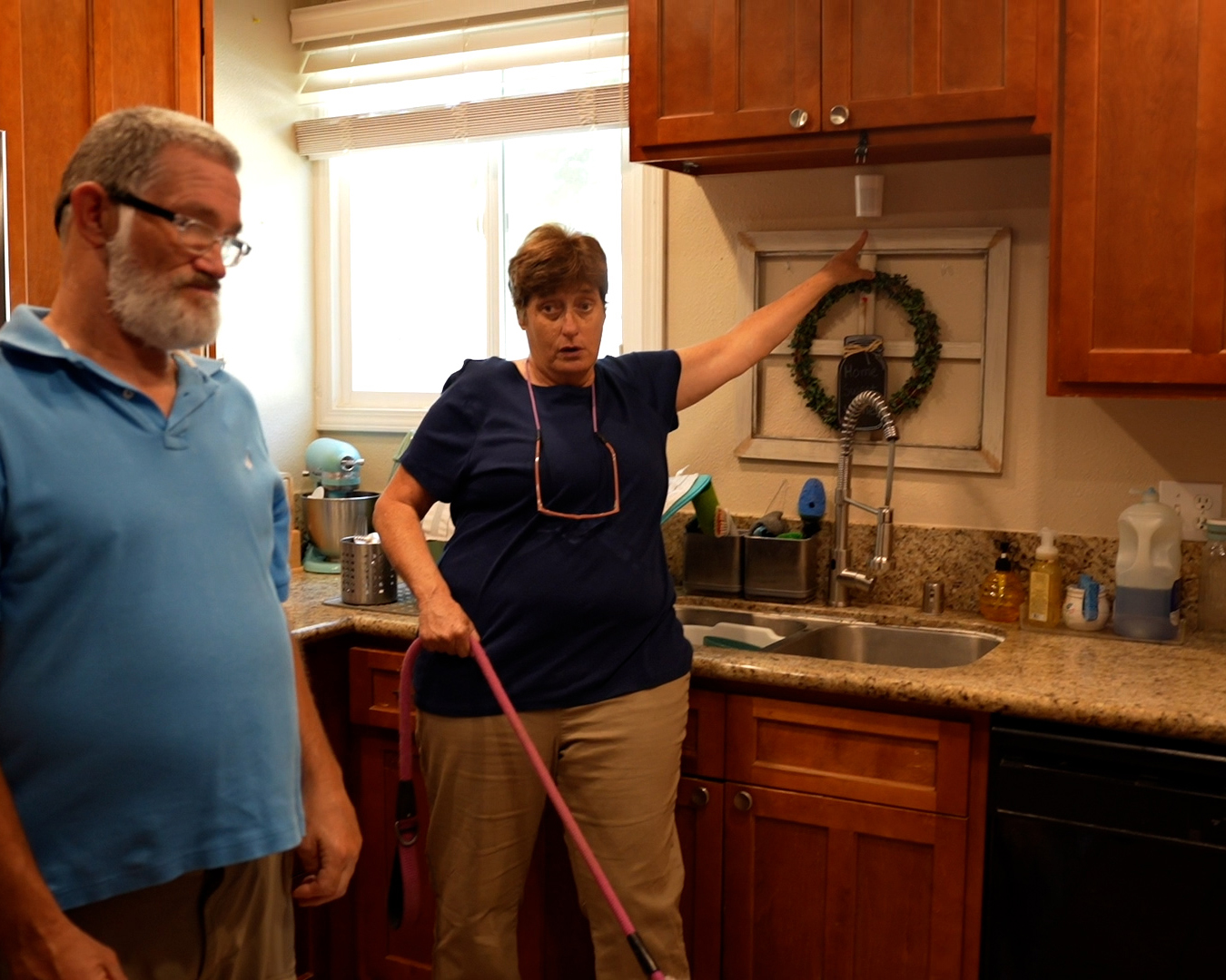 Man and woman stand in kitchen while she points at a light sensor under an upper cabinet.