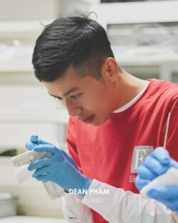 Young man wearing a red shirt cleans an object wearing blue latex gloves. The picture has the caption: Dean Phan, Tech, R&D