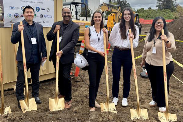 Two men and three women smile at the camera while holding shovels.