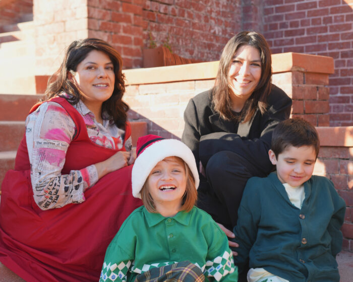 A family photo featuring two moms, a little wear wearing a Santa hat, and a little boy. 