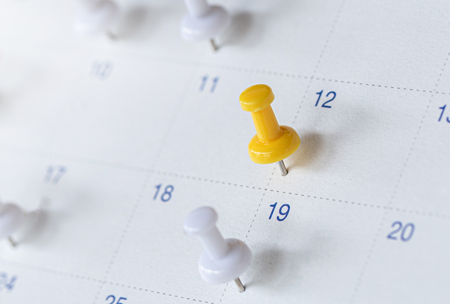 Yellow push pin marking a date on a calendar.
