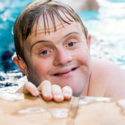 Person smiling in a swimming pool while holding on to the pool edge 