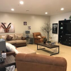 A spacious living room inside an ICF/DD home in Reseda. It features sofas and reclining chairs arranged around a coffee table, There is also a media console with a TV.